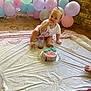 toddler, cake, balloons, birthday, party, plastic_cover, floor, sippy_cup, blue_frosting, rainbow_pattern, brick_wall, indoor, messy, celebration, child, food, sitting, clothing, cute, small_person