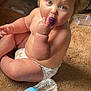 Willow is registered to the contest to win money with this photo: baby, child, diaper, indoor, carpet, water_bottle, metal_ball, curly_hair, blonde_hair, sitting, floor, toy, face, hand, person, curious, object, clutter, books, light