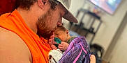 Matthew joined the competition — help win amazing prizes! man, baby, newborn, holding, kissing, blanket, tattoo, bracelet, cap, indoor, living_room, television, furniture, blurred_background, intimate, love, family, portrait, close_up, casual_clothing