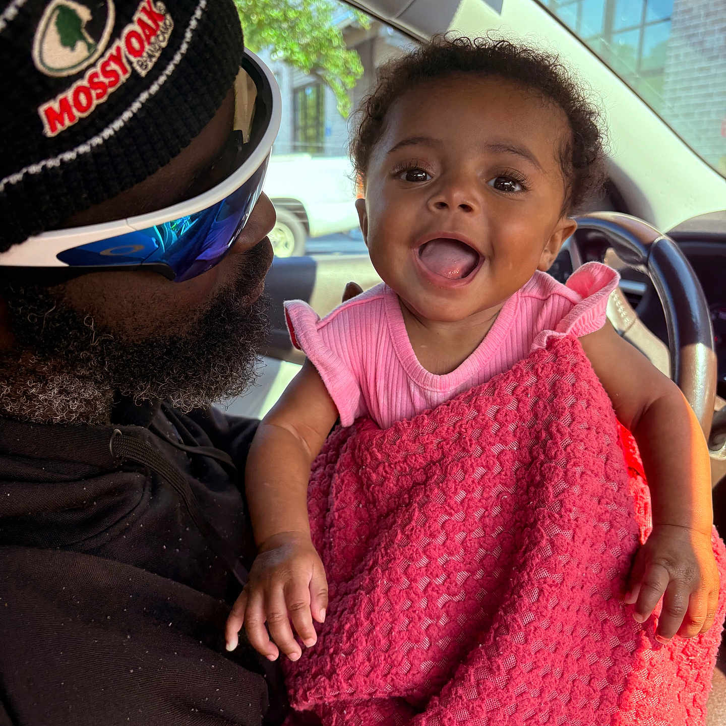 Yaleia is registered to the contest to win money with this photo: baby, child, person, man, beard, glasses, sunglasses, hat, clothing, blanket, car, car_interior, window, building, tree, smile, happy, holding, portrait, indoor