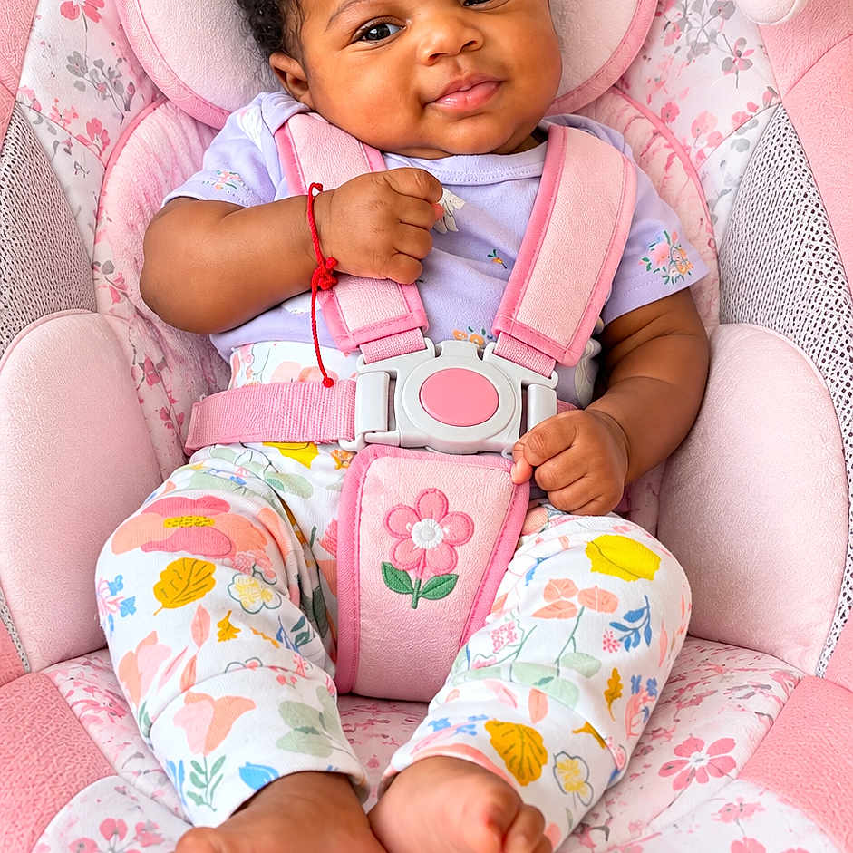Marlucia is registered to the contest to win money with this photo: baby, infant, child, smiling, sitting, bouncer, baby_chair, pink, floral, harness, curly_hair, bare_feet, toys, flower, colorful_clothing, portrait, indoors, carpet, happy, photography