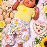 baby, child, infant, portrait, lying_down, smiling, floral, flowers, sunflowers, roses, daisies, teddy_bear, blanket, yellow_shirt, floral_pants, heart_sign, indoors, colorful, cute, photography