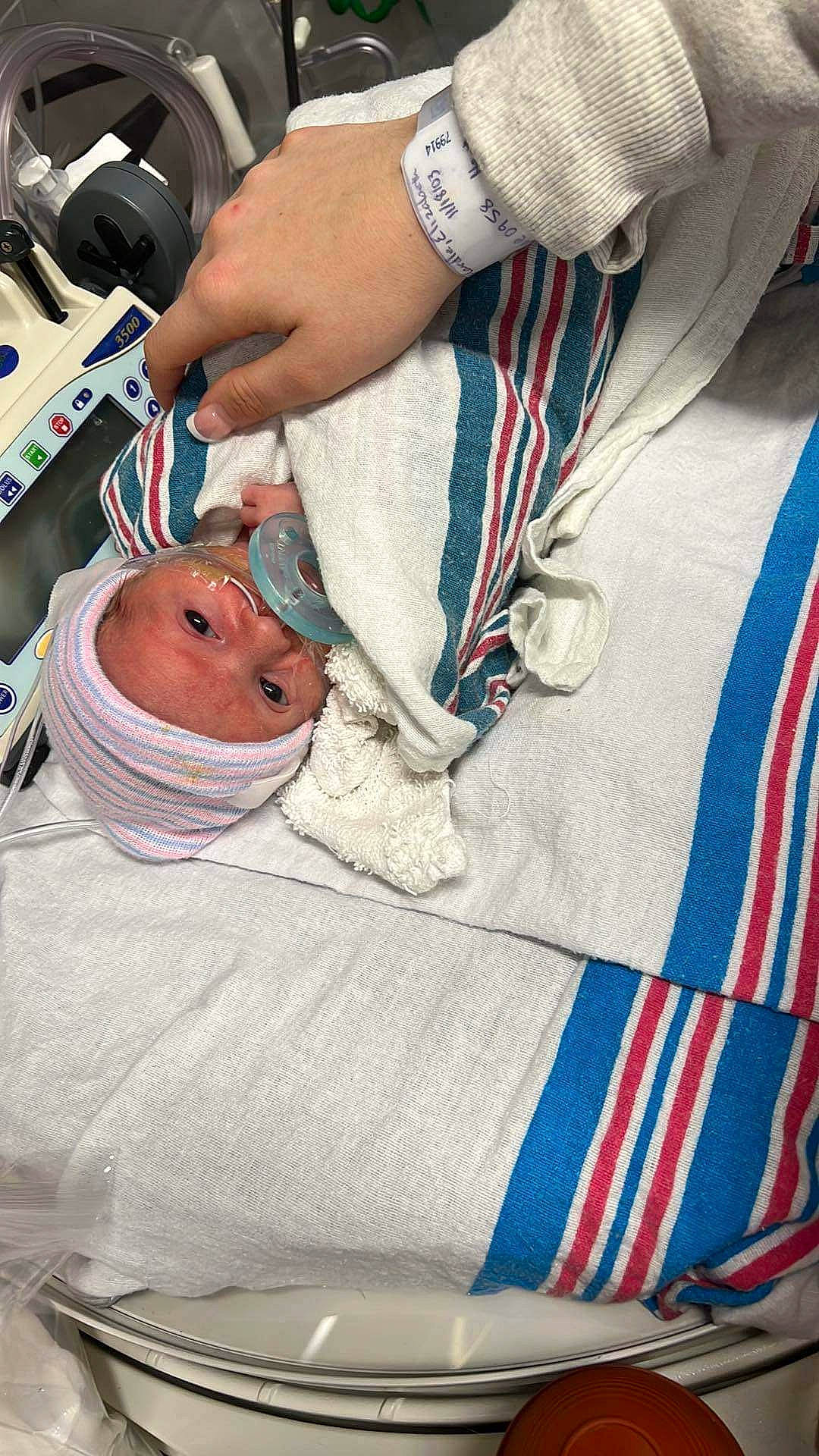 Camden is registered to the contest to win money with this photo: arm, baby, baby_products, child, comfort, event, finger, hand, hat, headwear, health_care, hospital, hospital_bed, linens, medical, medical_equipment, medical_procedure, patient, person, service