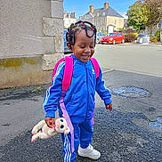 Romellia participe au concours pour gagner de l'argent avec cette photo : child, smiling, blue_tracksuit, white_sneakers, plush_toy, backpack, outdoor, street, happy, laughing, hair_ties, asphalt, building, car, daylight, urban, person, playful, cute, fashion