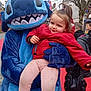 Elyna participe au concours pour gagner de l'argent avec cette photo : child, mascot, costume, blue, red_jacket, outdoor, street, person, face, smile, tree, pants, public, walking, people, winter_clothing, event, character, holding, fun