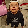 toddler, child, cap, hoodie, adidas, shoes, smile, indoor, tile_floor, chair, couch, blanket, person, young_child, cute, looking_up, casual_clothing, home_interior, face, standing