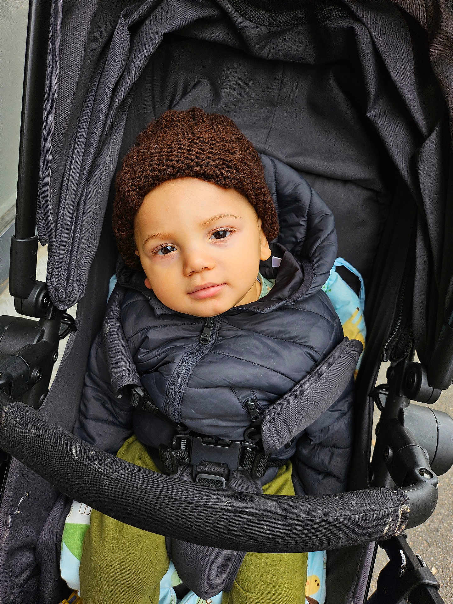 Chris-Emmanuel a rejoint le concours — aidez-le/la à gagner de superbes lots ! baby, casual, child, clothing, curious_expression, face, hat, infant, jacket, knit_hat, looking_at_camera, outdoor, person, puffy_jacket, safety_belt, seated, stroller, toddler, warm_clothes, young_child