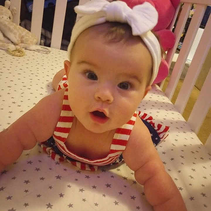Illeana joined the competition — help win amazing prizes! baby, bed, bow, child, crib, curious, cute, expression, face, furniture, headband, indoor, infant, pink_teddy_bear, portrait, reaching, room, stars_pattern, striped_clothing, toy
