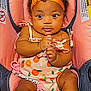 baby, infant, child, car_seat, orange_bow, orange_dress, pink, cute, clothing, face, hands, seat, straps, person, skin, headband, expression, indoors, sitting, young