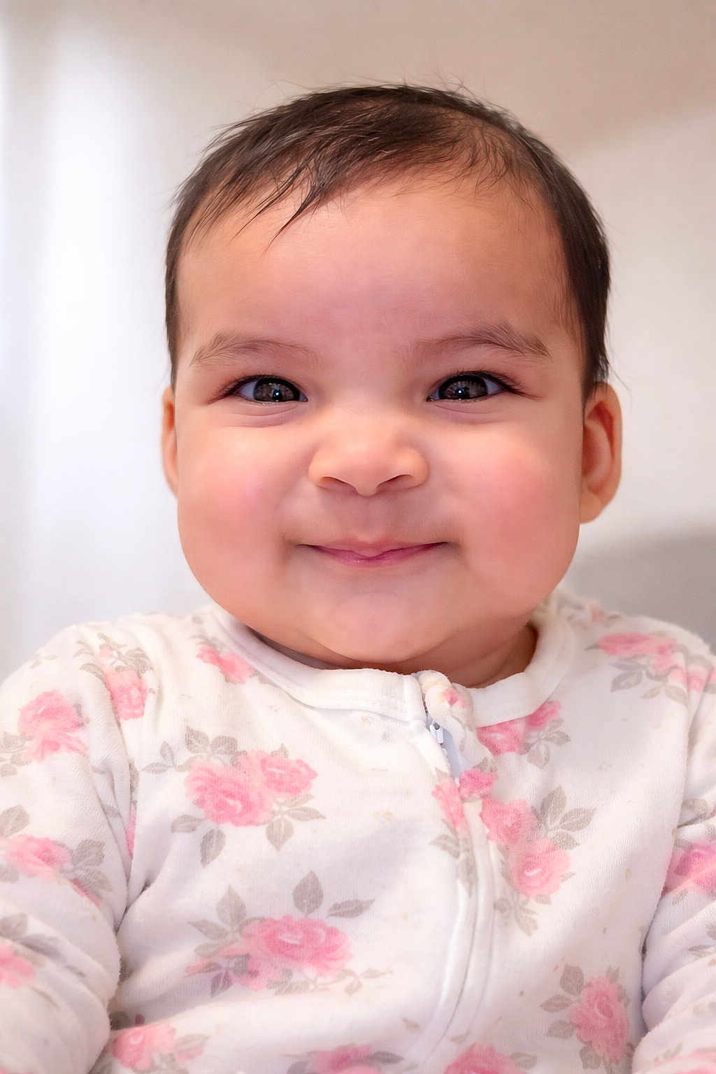 Larissa is registered to the contest to win money with this photo: baby, child, face, smile, onesie, clothing, pink, roses, cute, portrait, infant, cheeks, happy, eyes, indoor, person, young, soft_light, closeup, adorable