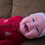 Floyd joined the competition — help win amazing prizes! baby, infant, child, smiling, red_onesie, white_hat, holiday_outfit, couch, upholstery, closeup, portrait, chubby_cheeks, open_mouth, eyes, cozy, fabric_texture, zipper, button, indoor, soft_lighting