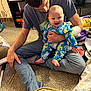 Floyd is registered to the contest to win money with this photo: baby, infant, man, adult, father, smiling, pajamas, sitting, lap, carpet, indoors, living_room, shelf, video_game_console, game_boxes, blanket, toy, hand, foot, cozy