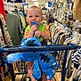 Westyn joined the competition — help win amazing prizes! baby, child, shopping_cart, plush_toy, clothing_store, clothes, rack, foot, chewing, green_bib, orange_shirt, blue_toy, aisle, shopping, indoor, retail, infant, cute, store, happy