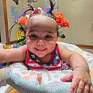 Braylee is registered to the contest to win money with this photo: baby, child, smiling, pigtails, flower, home_decor, indoor, person, colorful, happy, infant, face, arm, table, seat, clothing, cute, portrait, wooden_floor, baby_seat