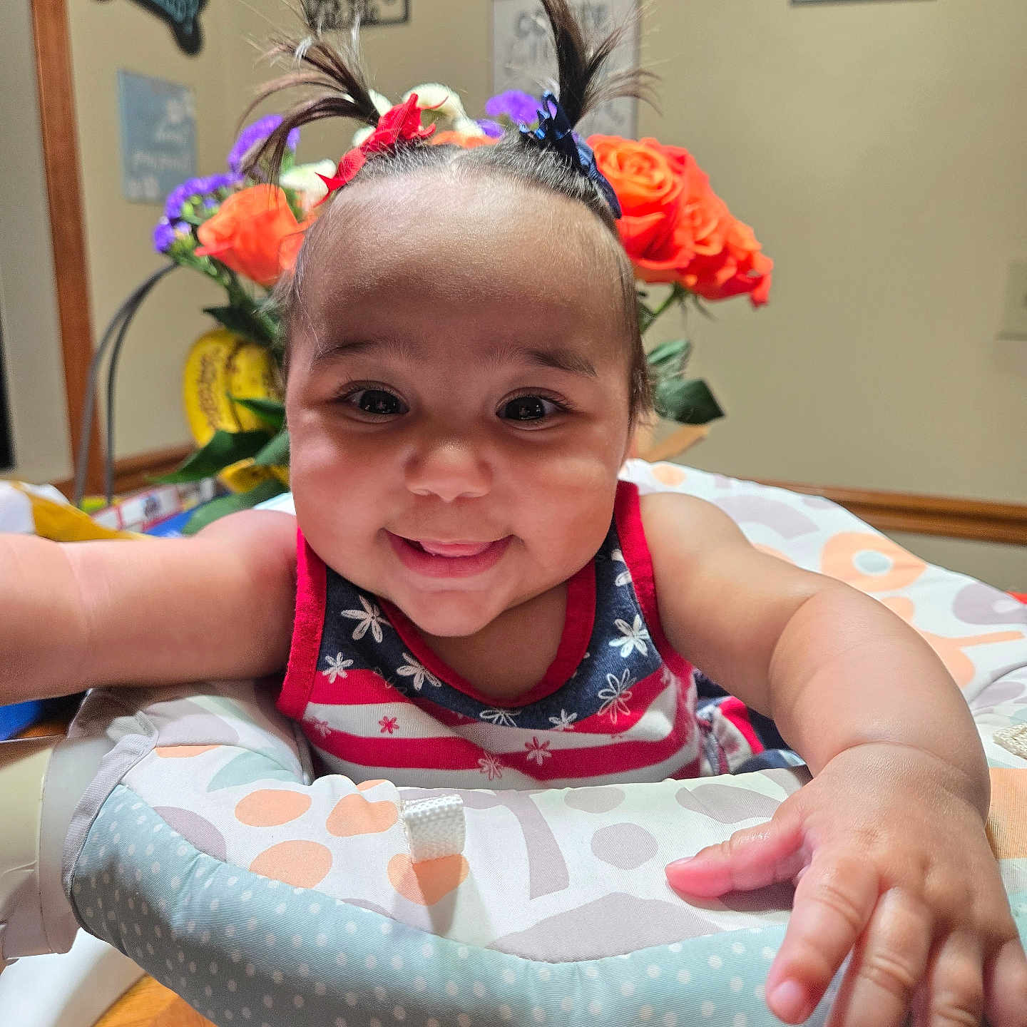 Braylee is registered to the contest to win money with this photo: baby, child, smiling, pigtails, flower, home_decor, indoor, person, colorful, happy, infant, face, arm, table, seat, clothing, cute, portrait, wooden_floor, baby_seat