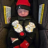 baby, car_seat, infant, sleeping, mittens, red_hat, red_socks, black_clothing, child, safety_harness, closeup, indoors, cute, newborn, face, headwear, hands, footwear, portrait, resting