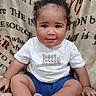 baby, child, smiling, sitting, tshirt, blue_shorts, socks, curly_hair, blanket, cozy, portrait, indoors, cute, happy, infant, person, face, young_child, warm, comfortable