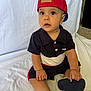 toddler, child, baby, red_cap, backwards_hat, black_polo, shorts, sandals, sitting, indoor, white_sheet, curious, brown_eyes, cute, portrait, young_child, footwear, hand, face, expression