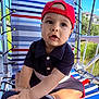 toddler, child, baby, cap, red_cap, navy_outfit, shoes, striped_chair, outdoor, daylight, porch, hand, face, sitting, curious, expression, summer, greenery, background, sunlight