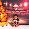 Akeem is registered to the contest to win money with this photo: toddler, child, basketball, inflatable, court, stadium, sports, book, reading, shoes, clothing, black_hair, smiling, indoor, floor, background, lights, seats, playful, portrait