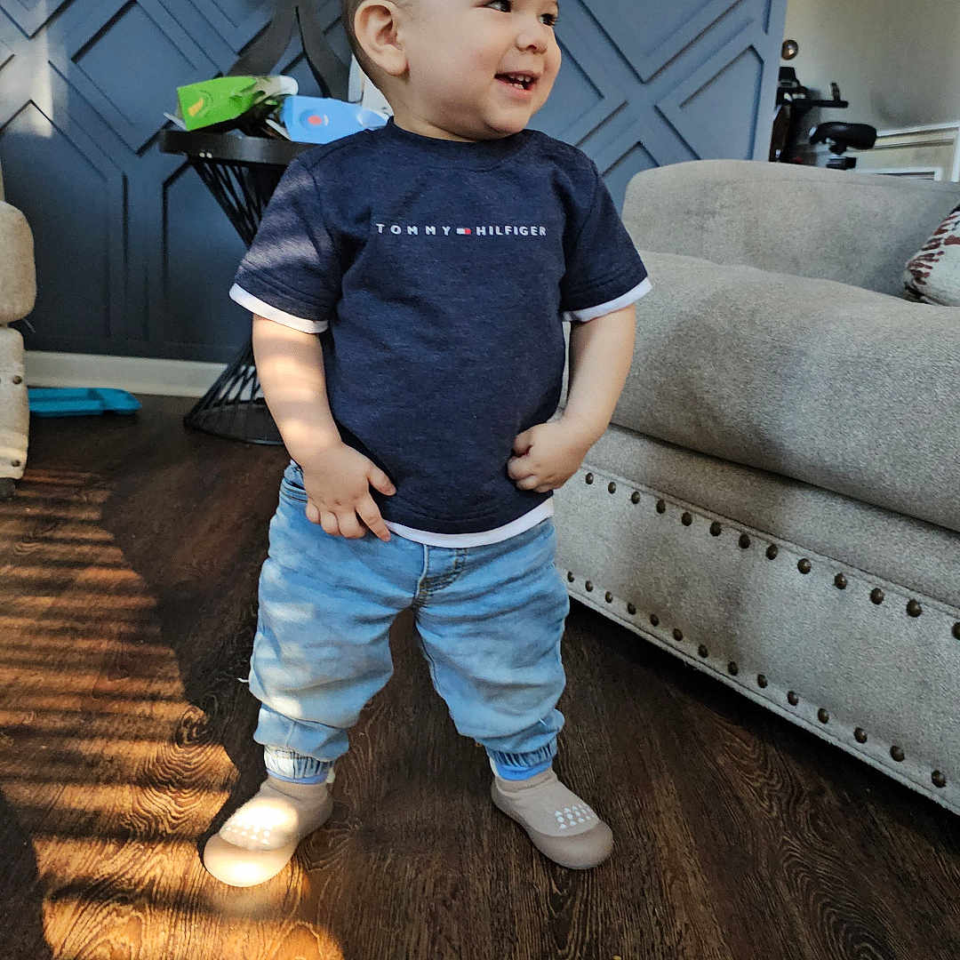 Liam joined the competition — help win amazing prizes! toddler, child, standing, smiling, indoor, living_room, couch, lamp, wooden_floor, jeans, shirt, shoes, sunlight, shadow, furniture, home, happy, person, casual_clothing, modern