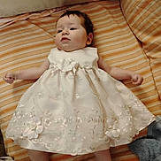 Holly joined the competition — help win amazing prizes! baby, child, dress, white_dress, floral, couch, striped, orange, beige, plush_toy, blanket, infant, lying_down, cute, soft, indoors, comfortable, calm, clothing, portrait