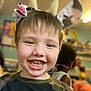 child, smiling, headband, cow_ears, flower, teeth, classroom, indoor, happy, boy, short_hair, camouflage_shirt, playful, cute, portrait, people, background_blur, kids, fun, education