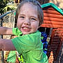 Zane is registered to the contest to win money with this photo: child, smiling, green_shirt, fence, playhouse, backyard, outdoor, daylight, happy, person, short_hair, young, casual_clothing, sunlight, nature, wood, leaves, blue_sky, play, fun