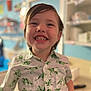 Zane joined the competition — help win amazing prizes! child, smiling, boy, dinosaur_shirt, indoor, happy, face, short_hair, teeth, casual_clothing, shelf, blurred_background, colorful_lights, portrait, cute, young, holding_object, playful, cheerful, person