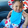 baby, child, hat, bib, clothing, person, indoor, car, seat, hand, face, skin, hair, beads, pattern, heart, stars, blue, red, white