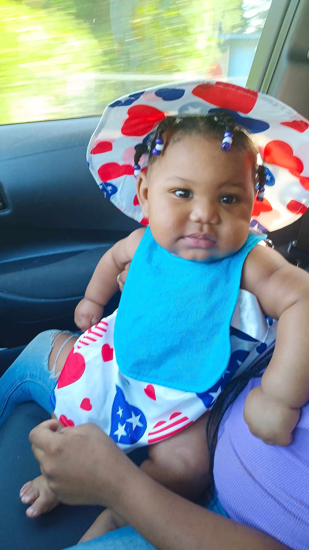Isabella joined the competition — help win amazing prizes! baby, child, hat, bib, clothing, person, indoor, car, seat, hand, face, skin, hair, beads, pattern, heart, stars, blue, red, white