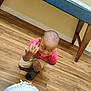 beige_shorts, boy, casual_clothing, child, crouching, expression, flooring, footwear, furniture, home, indoor, kid, motion_blur, person, playful, portrait, red_shirt, table, wooden_floor, young