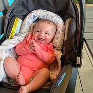 Stella is registered to the contest to win money with this photo: baby, infant, car_seat, smiling, happy, clapping_hands, blanket, pink_clothing, indoor, child, cute, young_child, seat, safety, car_seat_cushion, person, baby_girl, soft_lighting, wooden_floor, cozy