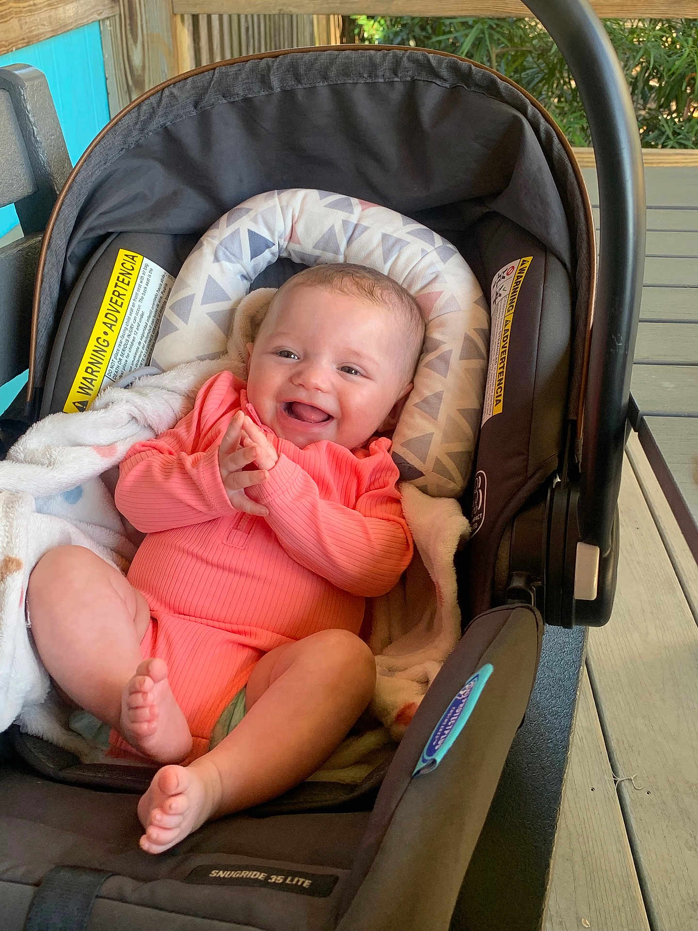 Stella is registered to the contest to win money with this photo: baby, infant, car_seat, smiling, happy, clapping_hands, blanket, pink_clothing, indoor, child, cute, young_child, seat, safety, car_seat_cushion, person, baby_girl, soft_lighting, wooden_floor, cozy