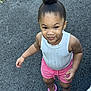 toddler, child, girl, standing, outdoor, asphalt, pink_shorts, white_top, crocs, hairstyle, bun, smile, playful, casual_clothing, feet, person, skin, young_child, summer_clothing, expression