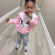 Ava is registered to the contest to win money with this photo: child, toddler, pink_jacket, jeans, sneakers, hair_buns, finger_in_mouth, necklace, hallway, wood_floor, baseboard, beige_wall, door, standing, portrait, indoor, cute, casual_photo, young_child, expression