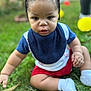 child, baby, toddler, braids, portrait, outdoor, grass, bib, socks, red_shorts, blue_shirt, sitting, close_up, chubby_cheeks, toy_ball, greenery, cute, face, eye_contact, skin