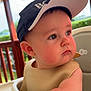 baby, child, high_chair, cap, outdoor, porch, wooden_railing, curious, face, skin, arm, infant, seat, sunlight, expression, closeup, person, clothing, headwear, daylight