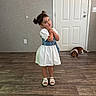child, cute, denim_vest, dog, door, dress, floor, footwear, girl, happy, indoor, mat, person, pet, pose, sandals, smile, wall, white_dress, wooden_floor