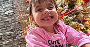 Jheselyn is registered to the contest to win money with this photo: celebration, cheerful, child, christmas_tree, cute_bunny_text, decorations, face, festive, happy, holiday_lights, home, indoor, joy, long_sleeve, ornaments, person, pink_sweatshirt, seasonal, smiling, toddler