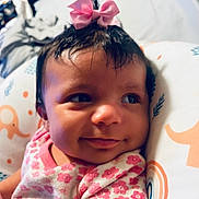 Gianna is registered to the contest to win money with this photo: baby, child, smile, pink_bow, floral_clothing, cushion, elephant_pattern, rainbow_pattern, face, portrait, indoors, cute, infant, resting, soft_lighting, closeup, cheeks, happy, young_child, headwear