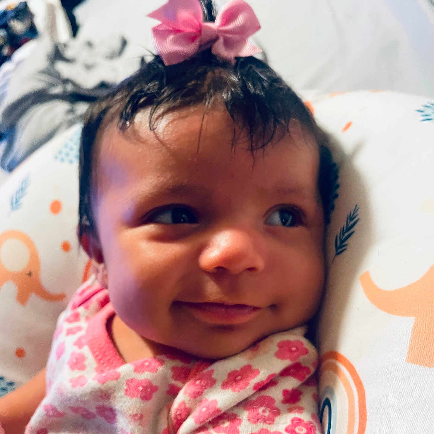Gianna is registered to the contest to win money with this photo: baby, cheeks, child, closeup, cushion, cute, elephant_pattern, face, floral_clothing, happy, headwear, indoors, infant, pink_bow, portrait, rainbow_pattern, resting, smile, soft_lighting, young_child