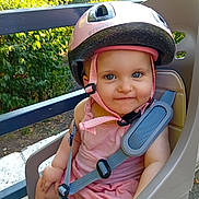 Helena participe au concours pour gagner de l'argent avec cette photo : baby, child, helmet, pink, blue_eyes, smile, child_bike_seat, straps, outdoor, greenery, safety, seat, person, summer, cute, infant, sunlight, headgear, happy, casual