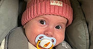 Mila participe au concours pour gagner de l'argent avec cette photo : baby, blanket, car_seat, child, clothing, cozy, cute, expression, eyes, face, hat, headwear, indoors, infant, pacifier, person, pom_poms, portrait, seatbelt, warm