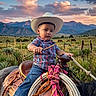 Jose Maria joined the competition — help win amazing prizes! child, toddler, cowboy_hat, horse, saddle, rope, plaid_shirt, jeans, boots, outdoor, sunset, mountains, field, grass, fence, rope_coil, riding, western, sky, nature