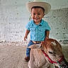 toddler, cowboy_hat, plaid_shirt, smiling_child, calf, animal, indoors, concrete_floor, white_wall, child, happy, boy, jeans, boots, rope, livestock, pet, farm, cute, young_child