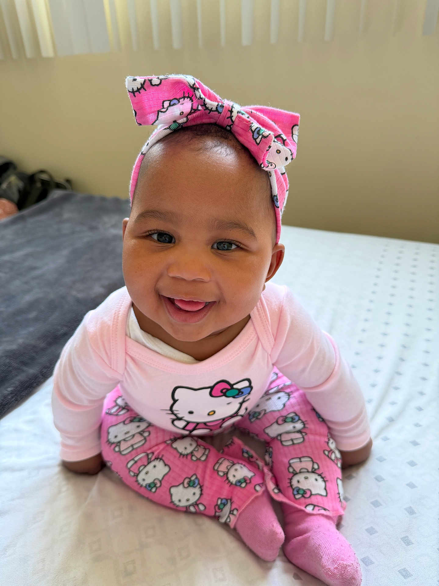 Nzuzo is registered to the contest to win money with this photo: baby, child, smiling, pink_clothing, headband, hello_kitty, sitting, bed, blanket, indoor, cute, happy, portrait, face, sock, person, infant, apparel, headwear, young_child