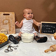 Victor joined the competition — help win amazing prizes! baby, apron, boots, flour, whisk, baking, bread, eggs, cutting_board, measuring_spoons, rolling_pin, doughnut, melon_pan, kitchen, cooking, smiling, child, sitting, food, playful