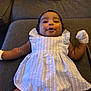 Kaeliah joined the competition — help win amazing prizes! baby, child, infant, dress, white_dress, mittens, couch, sofa, bottle, diaper_box, smiling, happy, indoor, furniture, person, cute, lying_down, skin, head, face