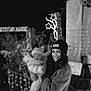 Paol participe au concours pour gagner de l'argent avec cette photo : woman, baby, child, smiling, hat, coat, night, outdoor, holiday_lights, festive, winter_clothing, holding, portrait, black_and_white, blurred_background, cheerful, warm, person, illumination, celebration
